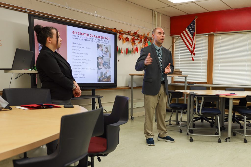 Doug Blanc (right) from the Arc Lexington is pictured speaking to a room of PTECH students (not pictured). A coworker is seen standing to his side.