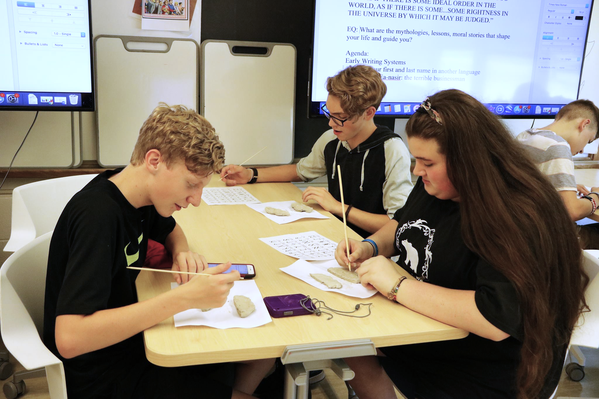 Three PTECH students are seated at a table doing school work.