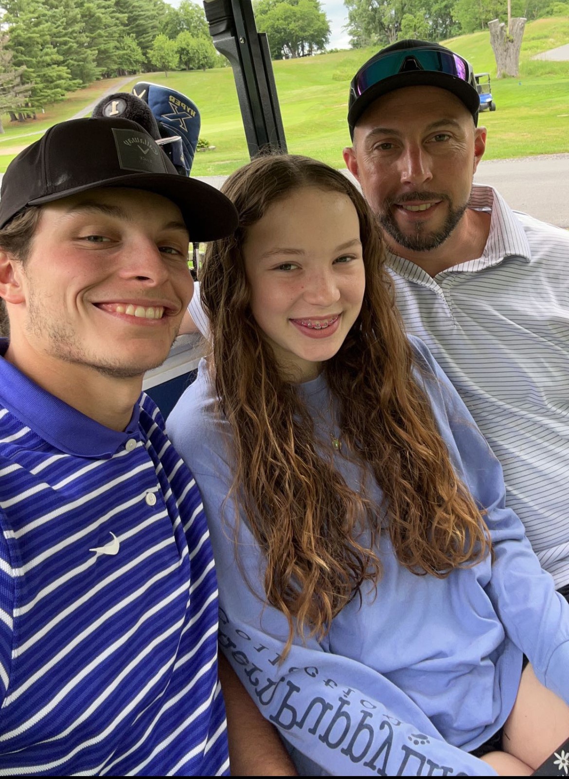 Pictured (left to right) are Frank Alvarez, his sister, and their father. They appear to be sitting in a golf cart. All are smiling. You can see what appears to be a golf course fairway in the background.