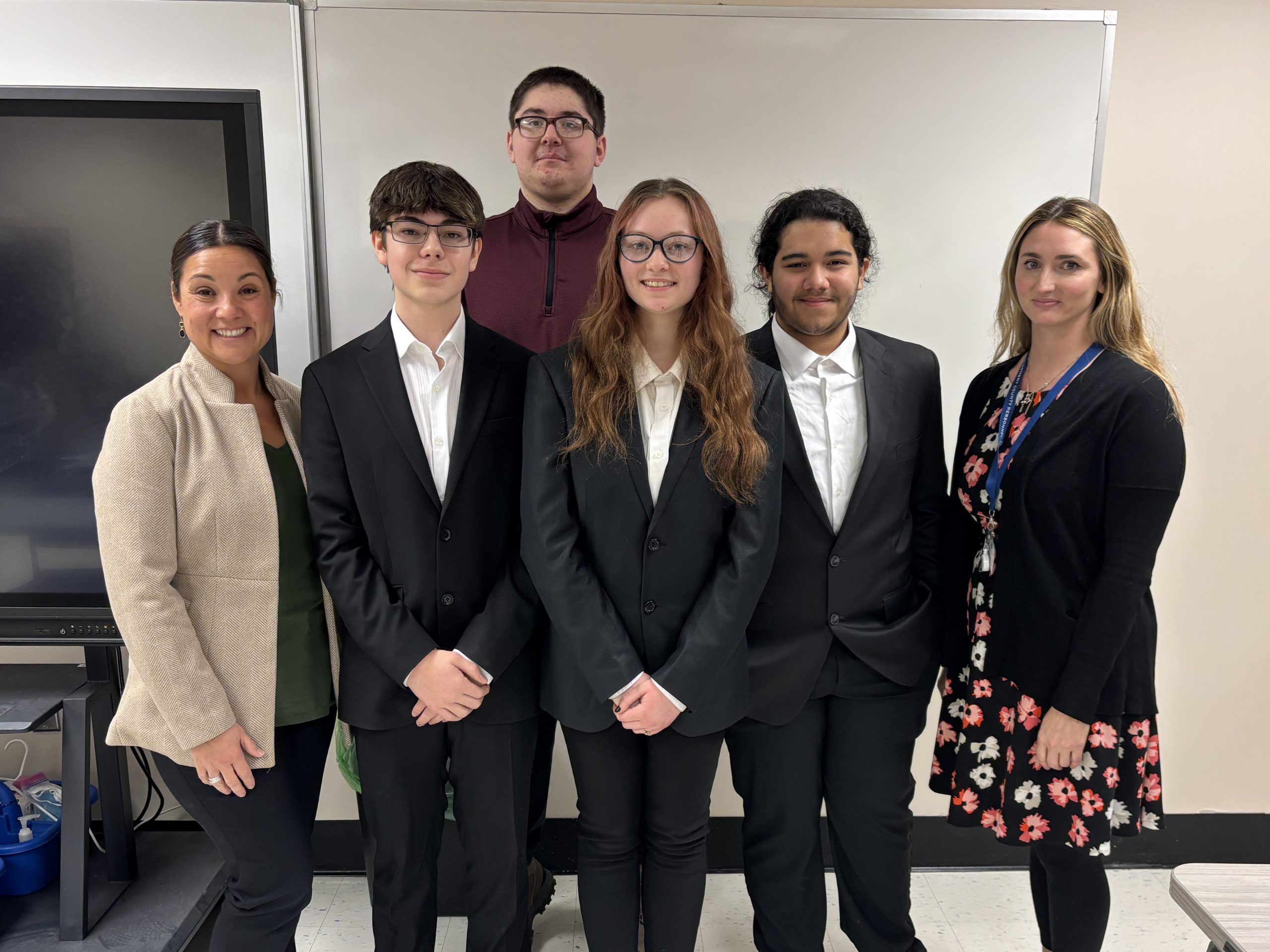 Four students and two business partners stand together wearing professional dress.